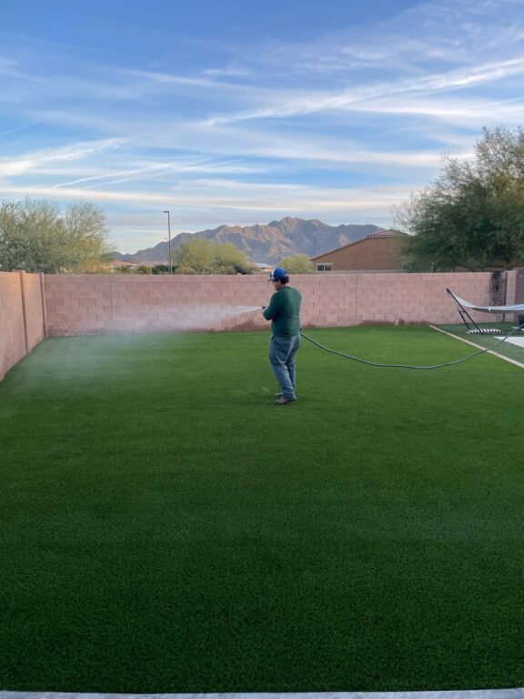 A man hoses down a synthetic grass backyard.
