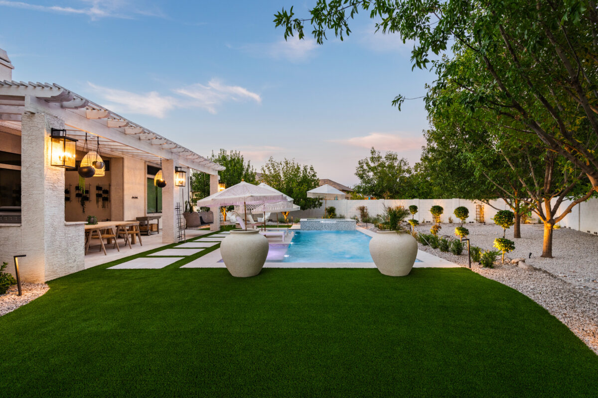 A luxury backyard in East Valley, Arizona, with synthetic grass, a modern swimming pool, outdoor living, and hardscaped walkway. Project by Alpine Turf.