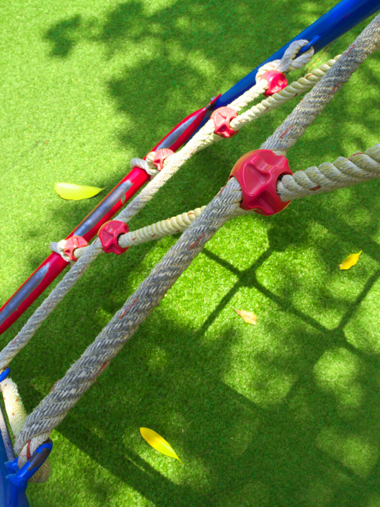 A top-down view of a kids' rope climbing grid leading down to a synthetic grass lawn.