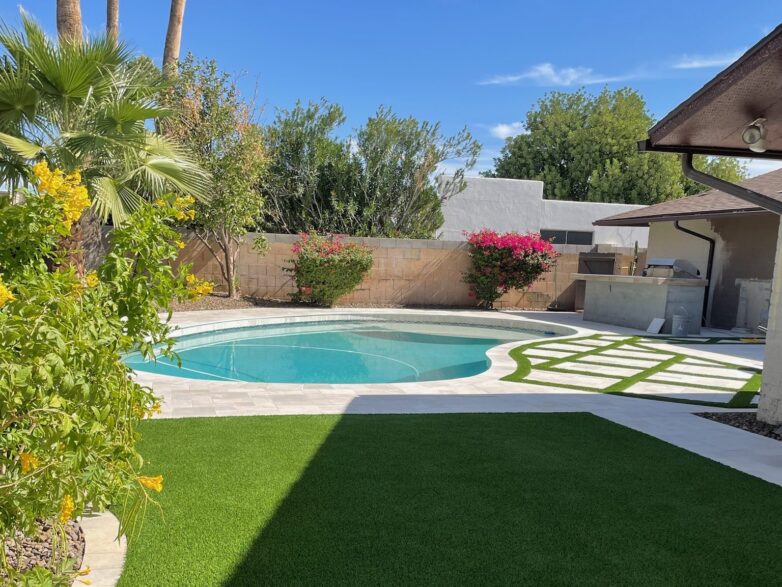 A backyard with a pool, synthetic grass lawn, and turf ribbons.