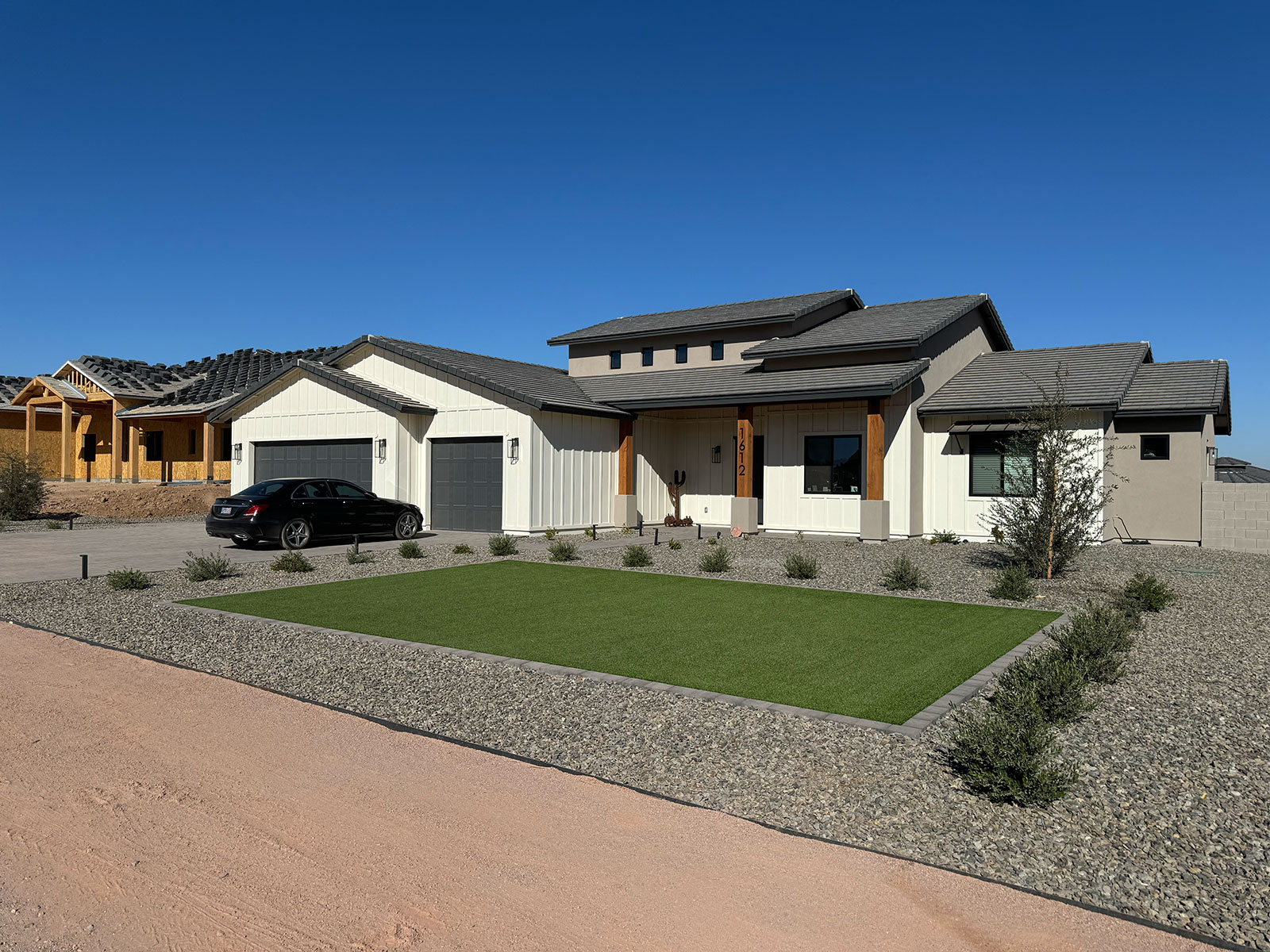 A modern, white home with a predominantly gravel front yard. Around the perimeter of the yard is desert-tolerant plants, with a rectangle of vibrant synthetic grass in the center.